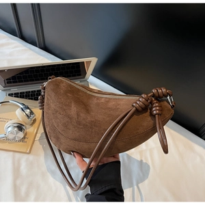 Detail view of a brown suede crescent bag with unique leather knot accents on the strap