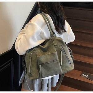Detailed street style view of dark green suede tote bag with multiple zipper pockets