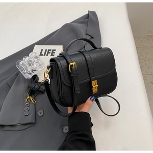 Close-up of black litchi grain leather bag with vintage gold metal lock on a suit