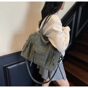 Detail view of large dark green tote bag featuring zip pockets and tassel accents