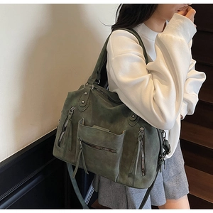 Model wearing dark olive green suede tote bag with fringe details and zippers on stairs
