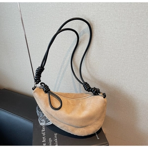 Detail view of light brown suede handbag featuring asymmetrical silhouette and knotted strap