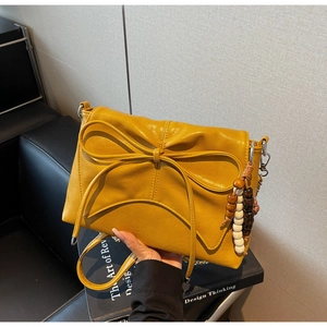 Detail of yellow crossbody bag featuring a large leather bow and vintage wooden beads