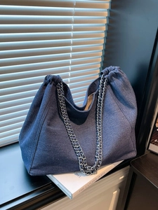 Große dunkelblaue Denim-Tote-Bag mit Kordelzug und Kettenriemen im weichen Sonnenlicht