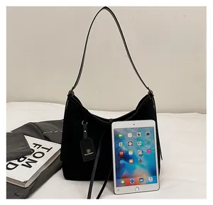 Size comparison of large black suede tote bag with wide shoulder strap on a bed