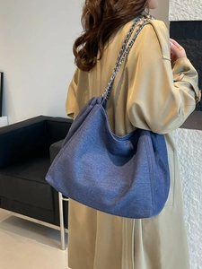 Große Denim-Tragetasche mit Kettenriemen am Modell über einem khakifarbenen Trenchcoat