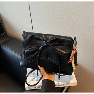 Close-up of black PU leather shoulder bag with bow knot and beaded chain detail