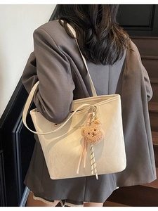 Chic beige tote bag with bear charm shown on model in a stylish urban indoor setting