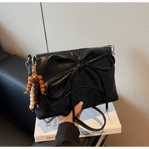 Detail of black bow shoulder bag with colorful wooden bead charm on a book