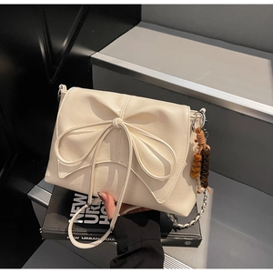 Close-up of off-white crossbody bag with large bow detail and beaded charm on stairs