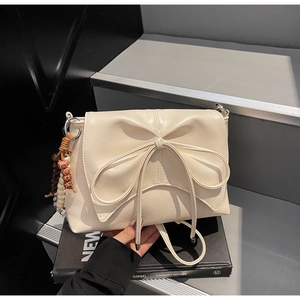 Close-up of cream crossbody bag with large bow decoration and wooden bead charm details