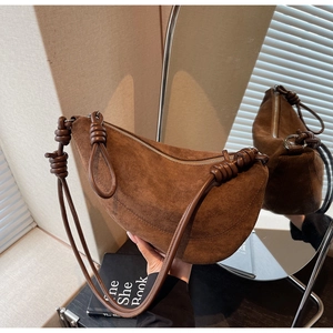 Detailed close-up of brown suede shoulder bag with elegant knot handle and silver metal zipper
