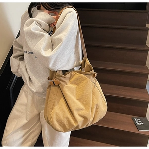 Detail of khaki nylon tote bag with buckle strap on wooden stairs shown by a model