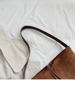 Detail of a brown suede bucket bag with a wide leather strap on a beige coat background