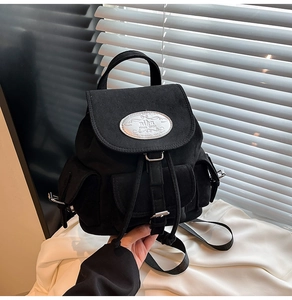 Détail d'un sac à dos noir mat multi-poches avec logo métallique ovale et rabat
