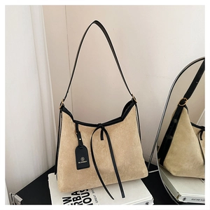 Detailed close-up of beige suede hobo bag with black leather trim and branded logo tag