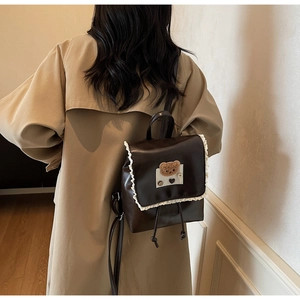 Detailed back view of a vintage brown leather backpack with lace trim and plush bear charm