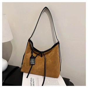Detail of tan suede tote bag with black leather strap and brand tag on a magazine