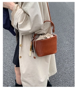 Detail of woven brown bucket bag with beaded charm and cream drawstring inner pouch