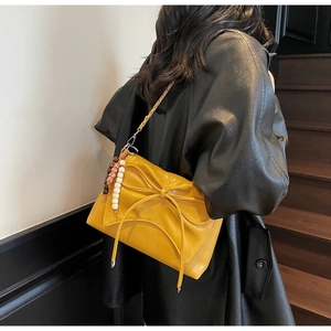 Detalle de bolso bandolera plisado amarillo con lazo y colgante étnico sobre la modelo
