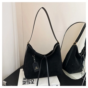 Detail of black suede tote bag with golden hardware and brand tag on a neutral background