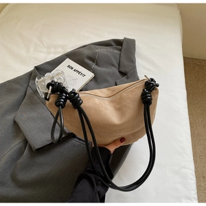 Detail of beige suede half-moon bag with decorative black knotted rope shoulder strap
