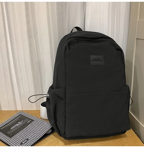 Close-up of minimalist black nylon backpack on a wooden table with side drawstring detail