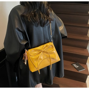 Detail of yellow bow shoulder bag with chain strap and wooden bead charm on a model