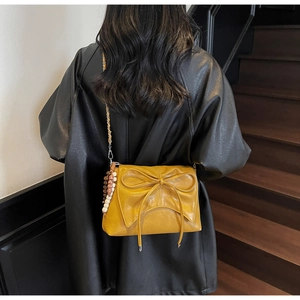 Detail of yellow bow shoulder bag featuring pleated texture and beaded charm accessory