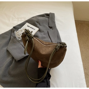 Detail of crescent shoulder bag featuring brown suede texture and green knotted rope strap