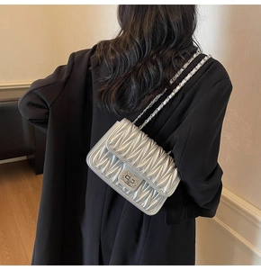 Silberne Stepptasche mit Wellenmuster und gewebtem Kettenriemen am Modell präsentiert