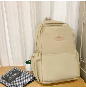 Detail of light beige laptop backpack showing leather logo patch and front zipper pocket