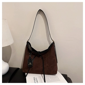 Detail of a brown suede tote bag featuring a black leather strap and brand logo tag