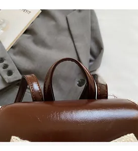 Detail of a brown leather backpack featuring reinforced handles and white lace edging trim