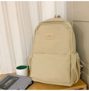 Macro detail of beige nylon backpack showing leather patch and durable matte texture
