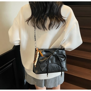 Close-up of black leather bow shoulder bag with chain strap and wooden bead charm