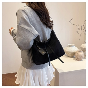 Detail of black suede tote bag with brand metal tag and decorative drawstring accents