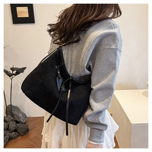 Detail of black suede hobo tote bag featuring long leather tassels and a metal logo tag