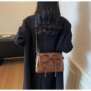 Detail of brown leather shoulder bag with bow knot and ethnic beaded charm on black coat