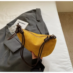 Detail of yellow crescent suede bag with knot strap on a grey blazer setting