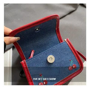 Detail showing blue denim mini bag with red edges, cherry embroidery and magnetic clasp