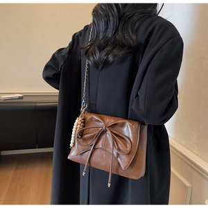 Detail of a brown bow shoulder bag with glossy leather, chain strap, and beaded charm