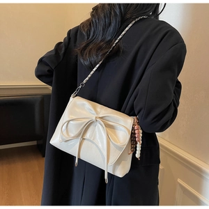 Modelo con bolso de hombro crema con lazo y cadena plateada, estilo oficina casual