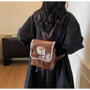 Detailed back view of a brown vintage leather backpack with lace trim and plush bear decor