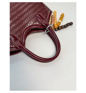 Détail du sac seau tressé bordeaux montrant le motif et le pendentif en perles