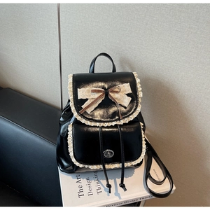 Détail d'un sac à dos noir en cuir avec bordure en dentelle blanche et nœud beige