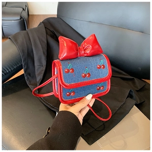 Detail of denim mini bag featuring cherry embroidery and a large red glossy bow decor