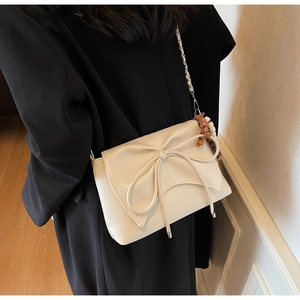 Close-up of cream leather shoulder bag featuring a large bow and beaded charm on model