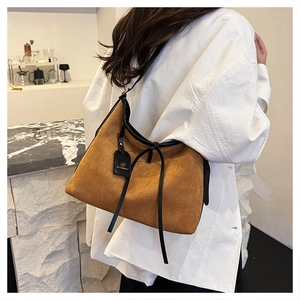 Brown suede tote bag side view on shoulder with black leather trim and tassel detail