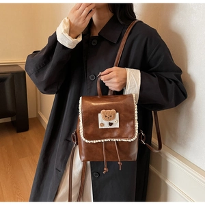 Close-up of brown leather backpack with teddy bear embroidery and lace trim details